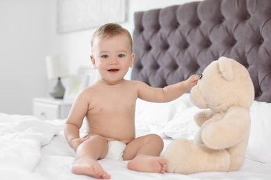 Photo of Adorable little baby with teddy bear on bed at home