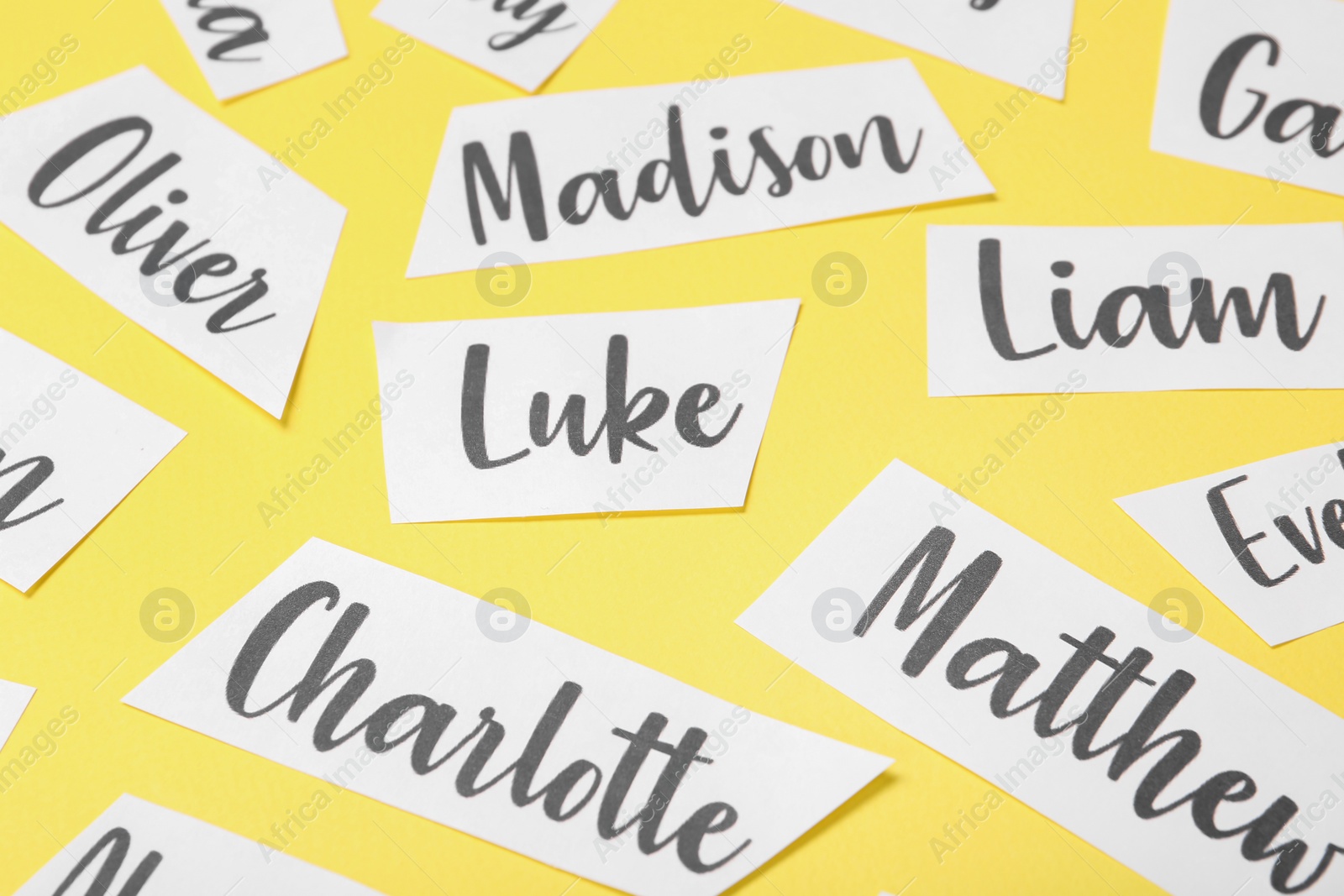 Photo of Paper sheets with written different baby names on yellow background, closeup