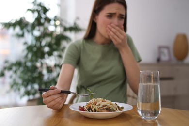 Photo of Young woman feeling nausea while eating at wooden table indoors. Toxicosis during pregnancy