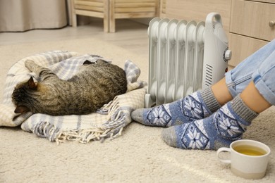 Young woman and cute tabby cat near electric heater at home, closeup