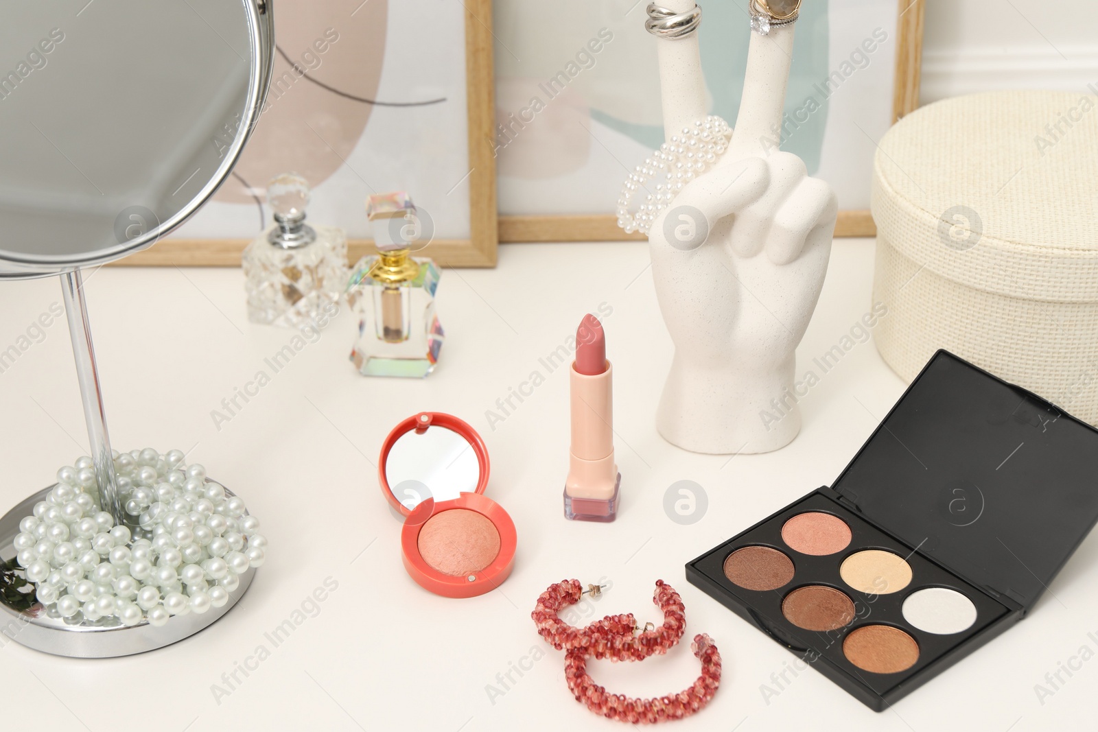 Photo of Mirror, cosmetic products, perfumes and jewelry on white dressing table, closeup