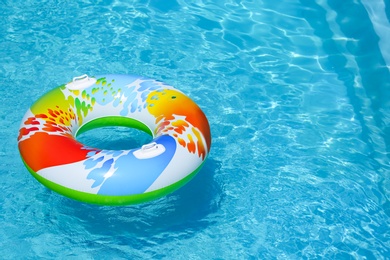 Colorful inflatable ring floating in swimming pool on sunny day. Space for text