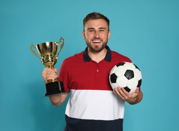 Photo of Portrait of happy young soccer player with gold trophy cup and ball on blue background
