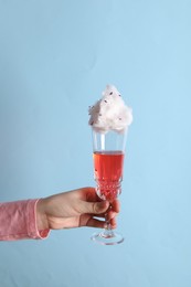 Photo of Woman holding glass of cotton candy cocktail on light blue background, closeup
