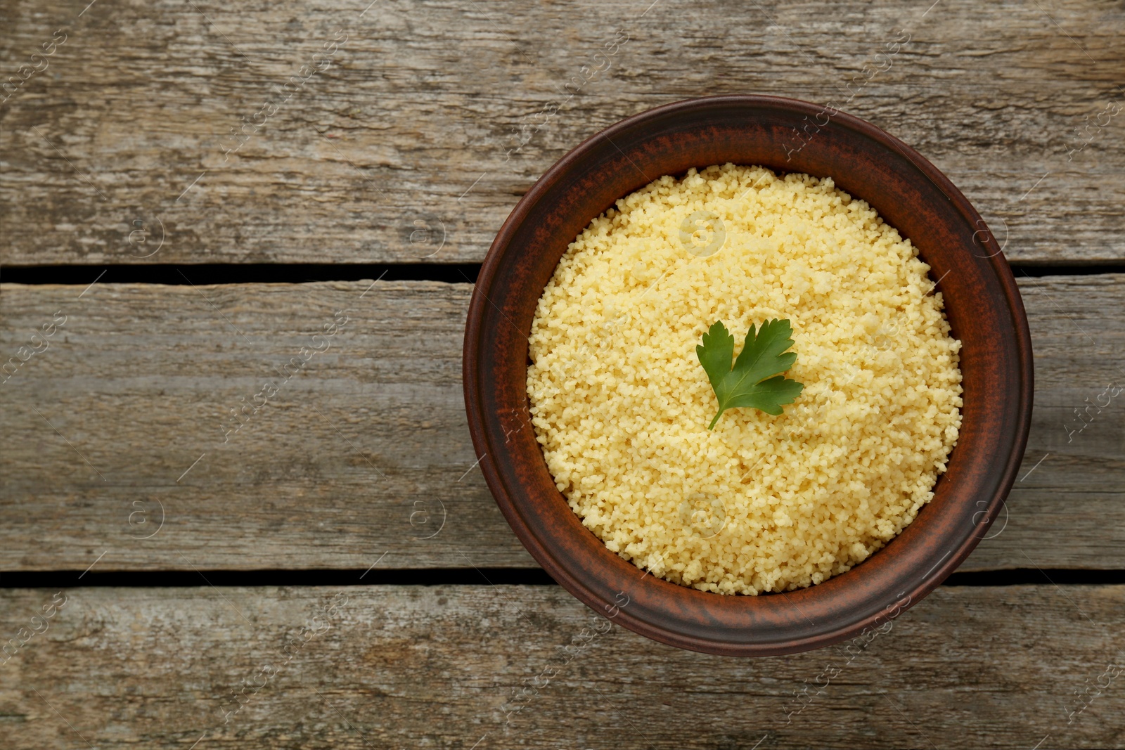 Photo of Tasty couscous with parsley on wooden table, top view. Space for text