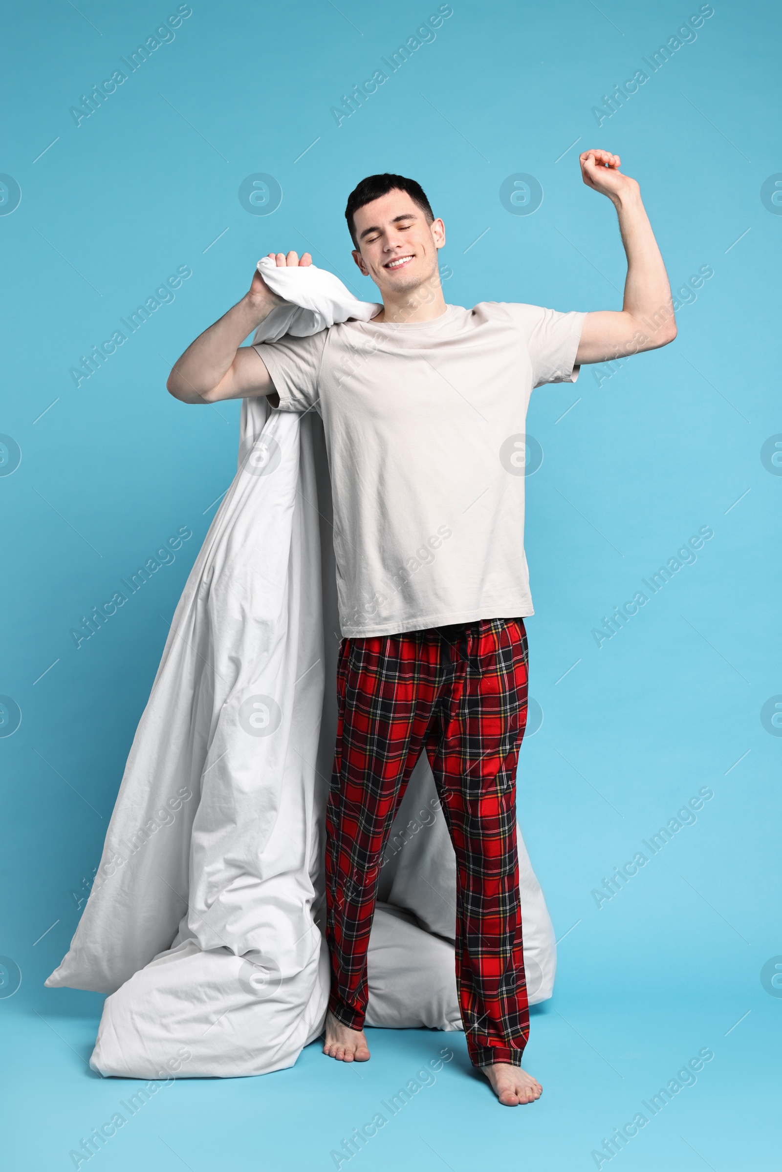 Photo of Happy man in pyjama holding blanket on light blue background