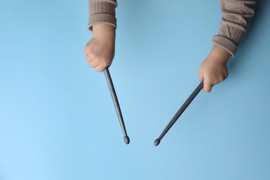 Photo of Little kid holding drumsticks on light blue background, top view