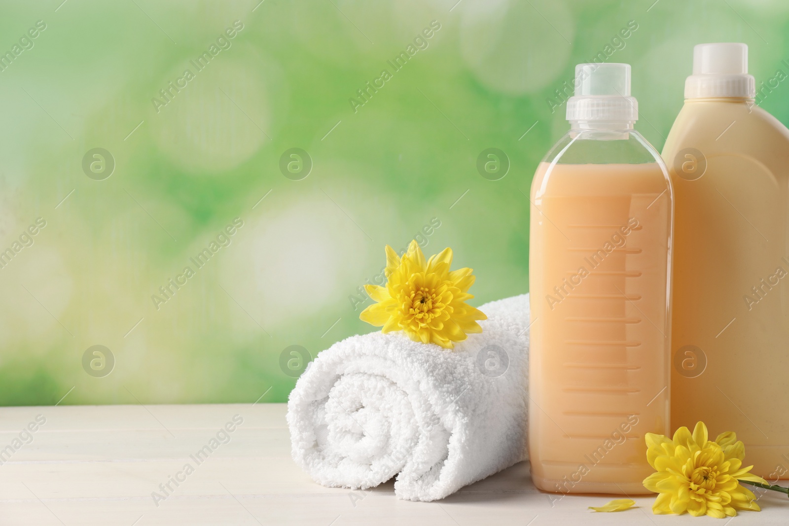 Photo of Bottles of laundry detergents, towel and beautiful flowers on white wooden table. Space for text