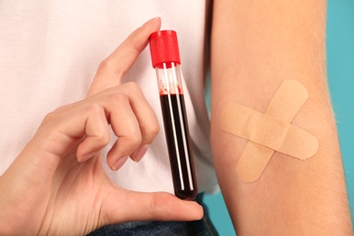 Woman holding test tube near hand with adhesive plasters against color background, closeup. Blood donation
