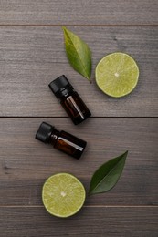 Photo of Bottles of essential oil with lime slices and leaves on wooden table, flat lay