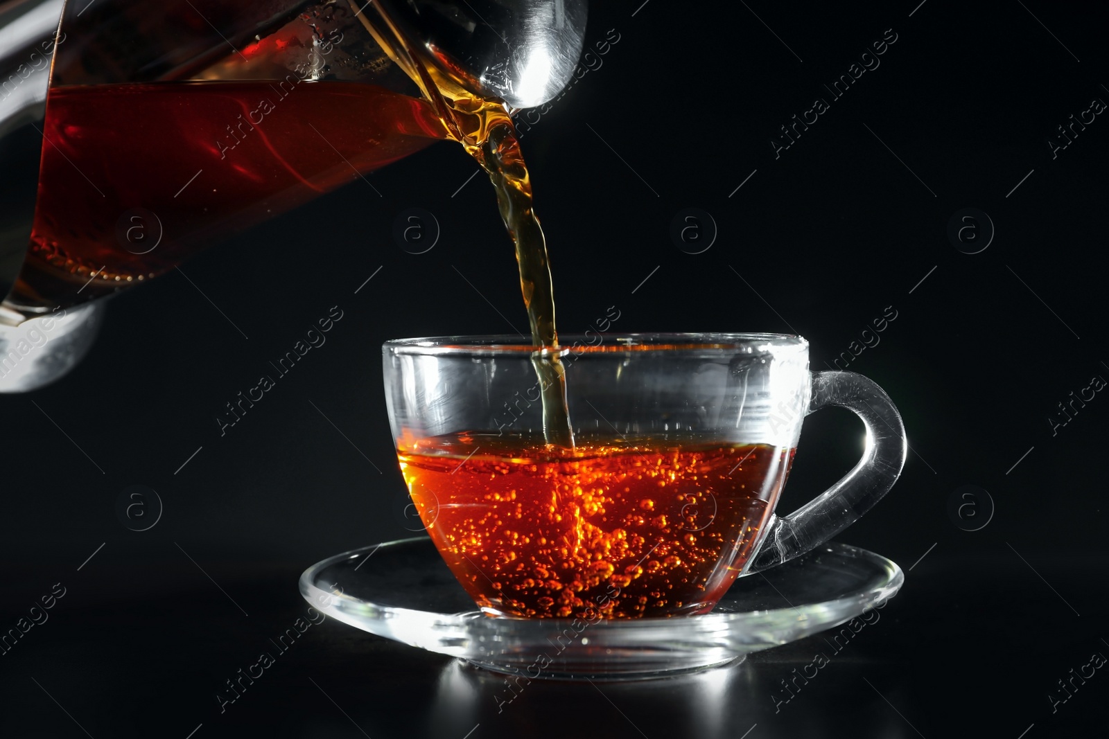 Photo of Pouring hot tea into glass cup on dark table