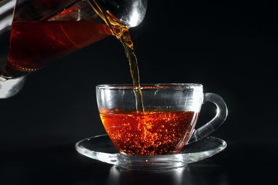 Pouring hot tea into glass cup on dark table