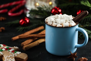 Delicious hot chocolate with marshmallows and cocoa sticks near Christmas decor on black table, closeup. Space for text