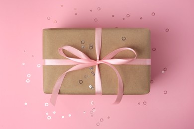 Photo of Beautiful gift box with bow and confetti on pink background, top view