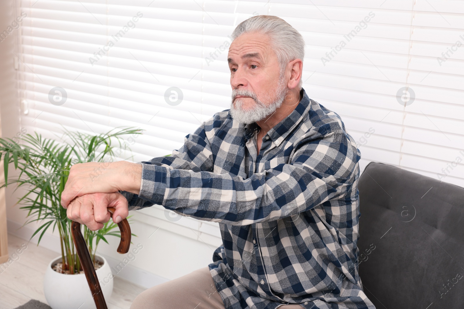 Photo of Senior man with walking cane sitting on armchair at home