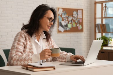 Photo of Woman with modern laptop and cup of tea learning at home