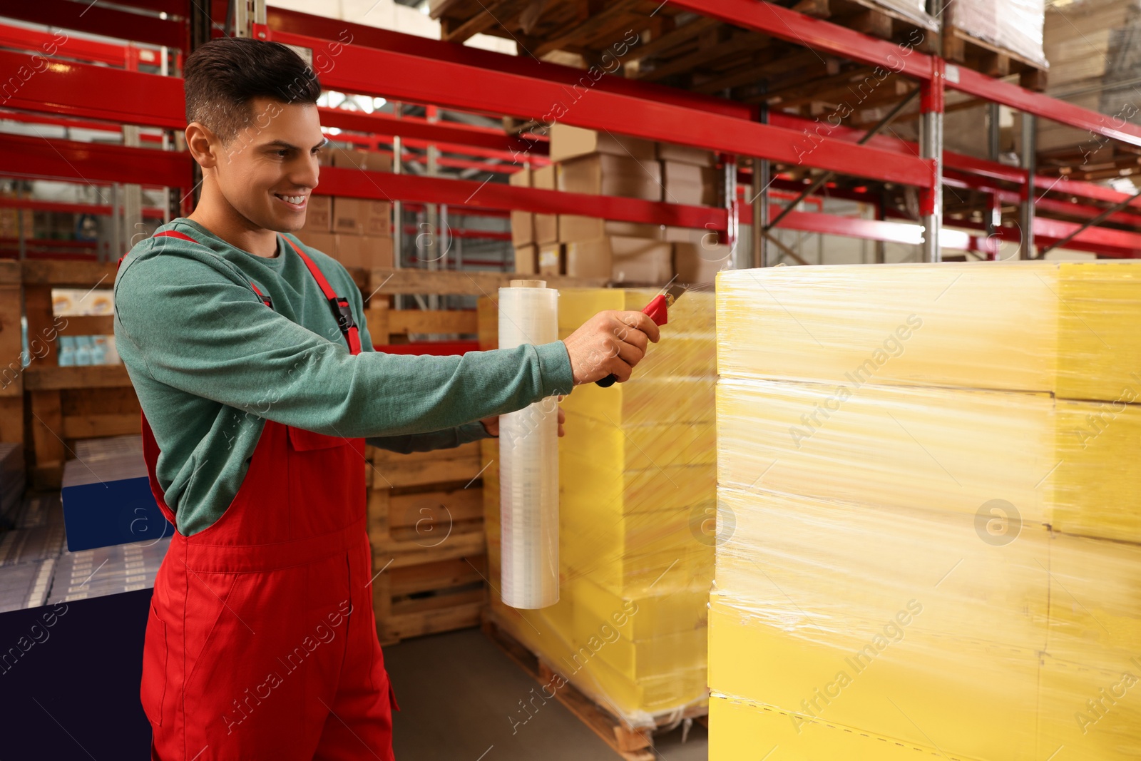 Photo of Worker wrapping boxes in stretch film at warehouse