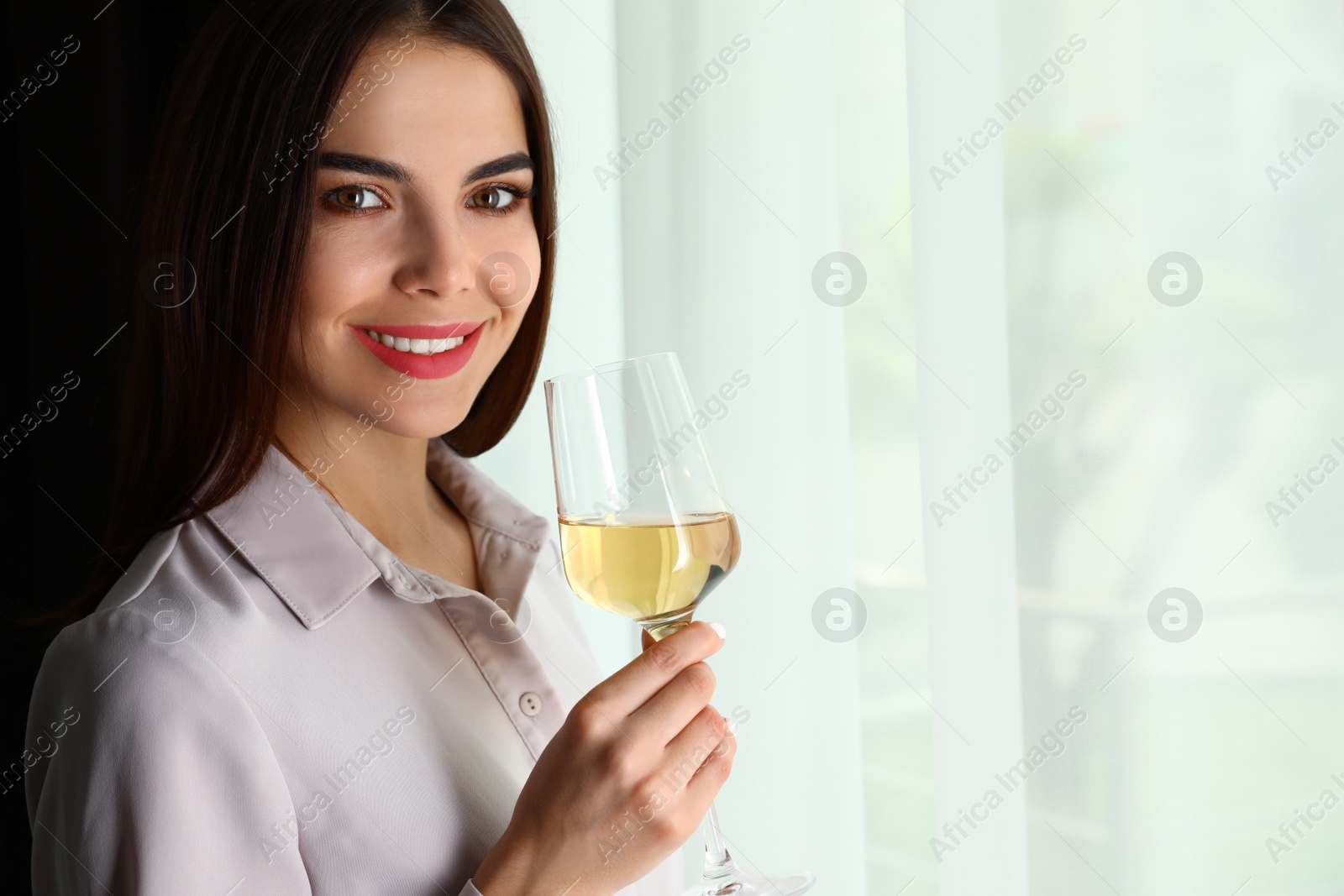 Photo of Beautiful young woman with glass of luxury white wine indoors. Space for text