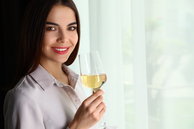 Beautiful young woman with glass of luxury white wine indoors. Space for text