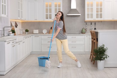 Photo of Enjoying cleaning. Woman in headphones listening music and mopping in kitchen