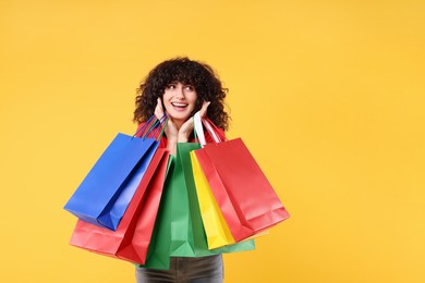 Happy young woman with shopping bags on yellow background. Space for text