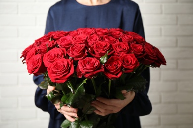 Photo of Woman holding luxury bouquet of fresh red roses near white brick wall, closeup