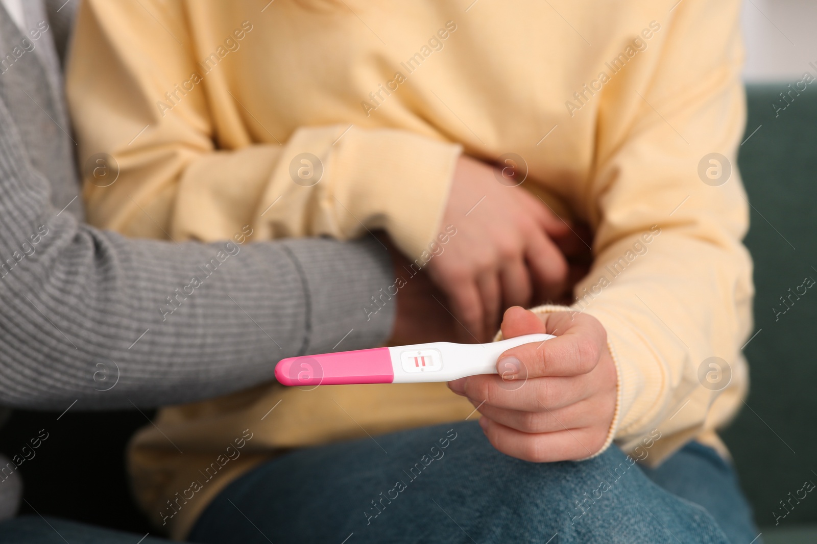 Photo of Young woman showing her mother pregnancy test, closeup. Grandparent reaction to future grandson