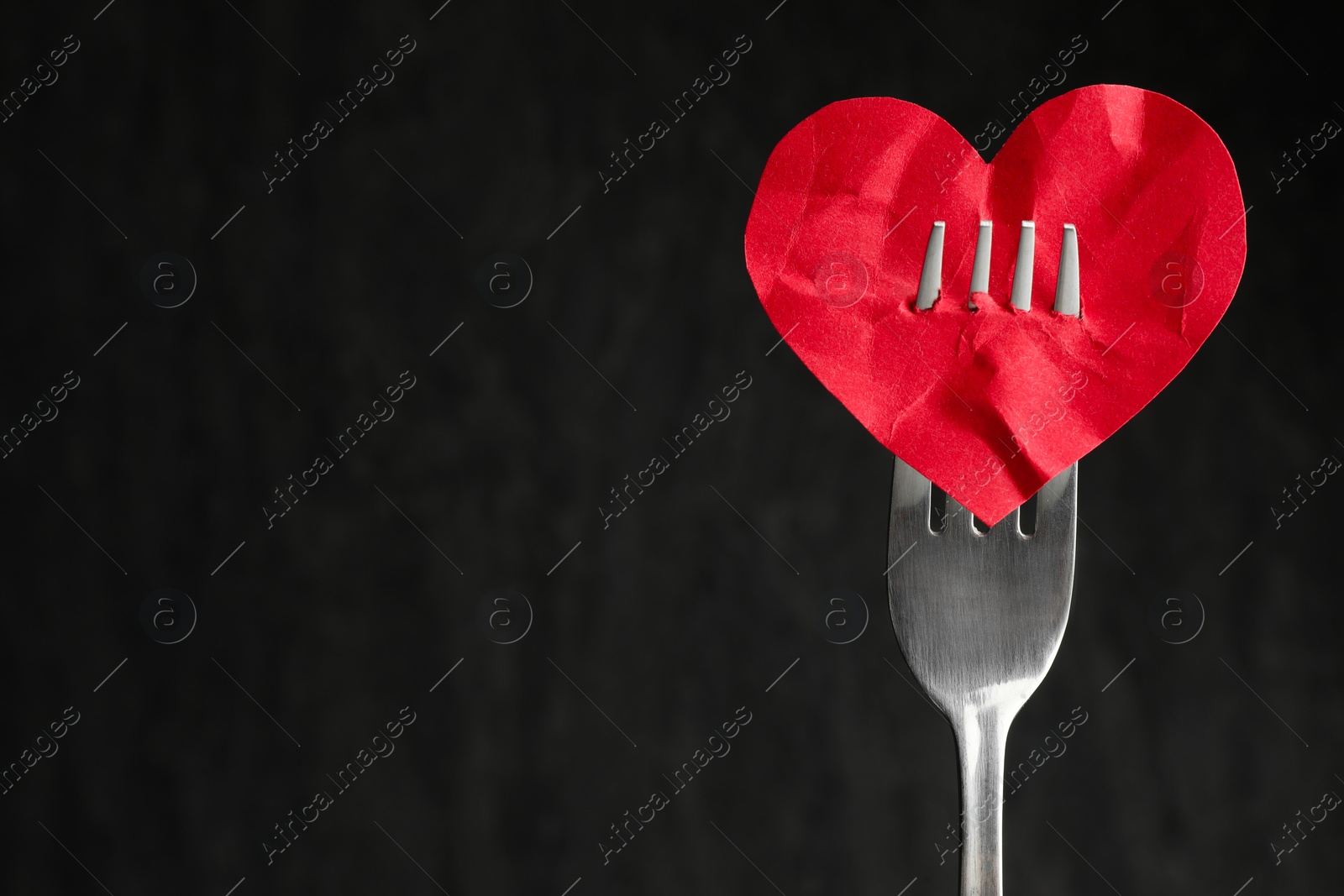 Photo of Broken heart. Red paper heart pierced with fork against black background, closeup. Space for text