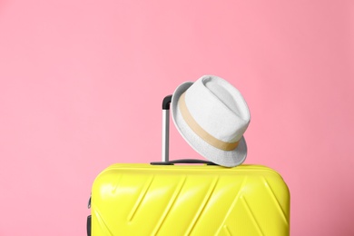 Photo of Modern yellow suitcase and hat on light pink background