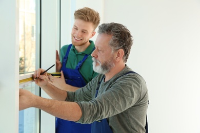 Service men measuring window for installation indoors