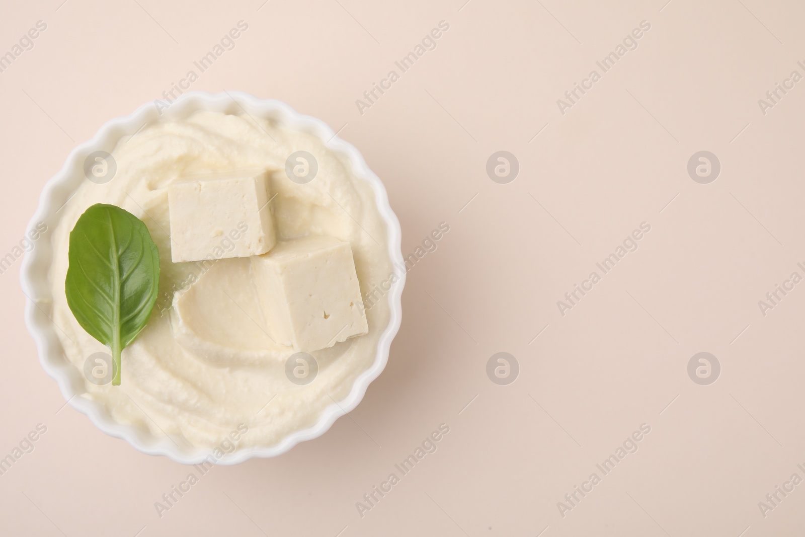 Photo of Delicious tofu sauce and basil leaf in bowl on beige background, top view. Space for text