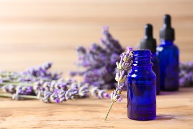 Bottle with essential oil and lavender flowers on wooden table. Space for text