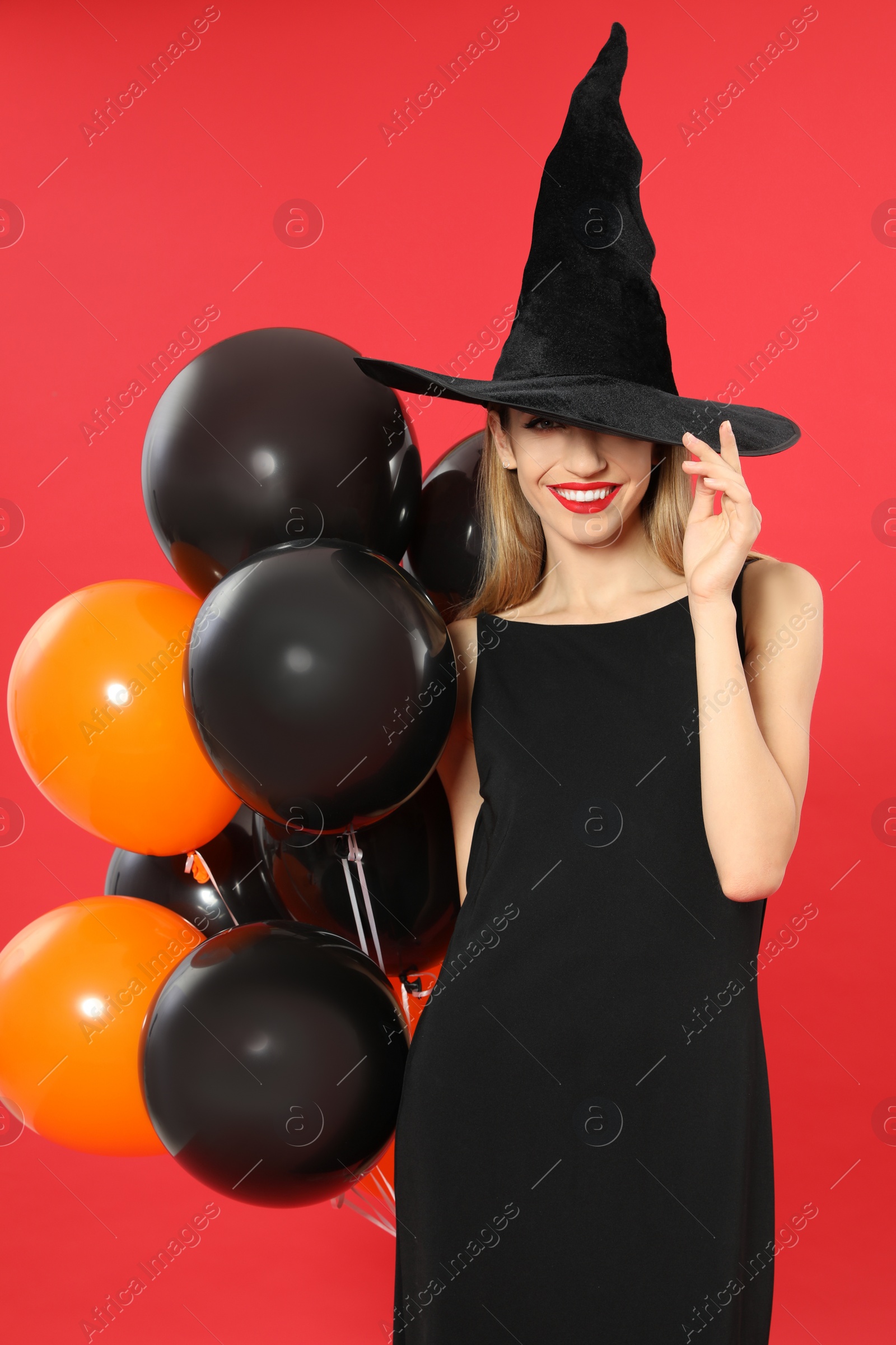 Photo of Beautiful woman wearing witch costume with balloons for Halloween party on red background