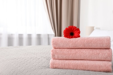 Photo of Stack of fresh towels with flower on blanket in bedroom. Space for text