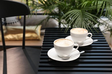 Ceramic cups of aromatic coffee with foam on wooden table in cafe. Space for text