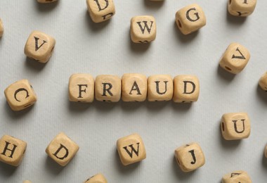 Word Fraud of wooden cubes with letters on grey background, flat lay