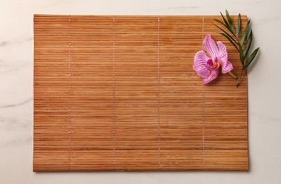 Photo of Bamboo mat, green leaf and orchid flower on white marble table, top view. Space for text
