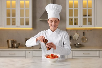 Professional chef adding pepper into delicious dish at white marble table in kitchen