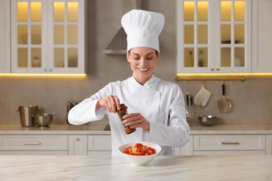 Photo of Professional chef adding pepper into delicious dish at white marble table in kitchen