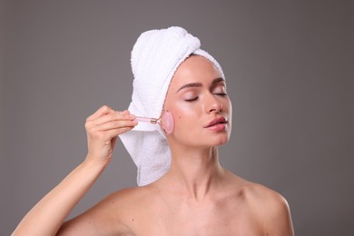 Photo of Young woman massaging her face with rose quartz roller on grey background