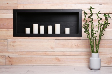 Vase with green bamboo near candles on shelf indoors