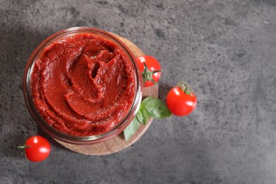 Photo of Jar of tasty tomato paste and ingredients on grey textured table, flat lay. Space for text