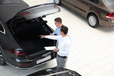 Photo of Young salesman working with client in modern car dealership, above view