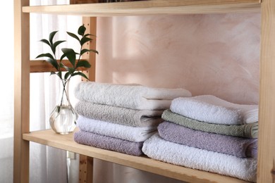 Photo of Stacked soft towels and green leaves on wooden shelf indoors