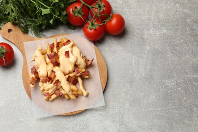 Delicious French fries with bacon, cheese sauce, tomatoes and herbs on light grey table, top view. Space for text