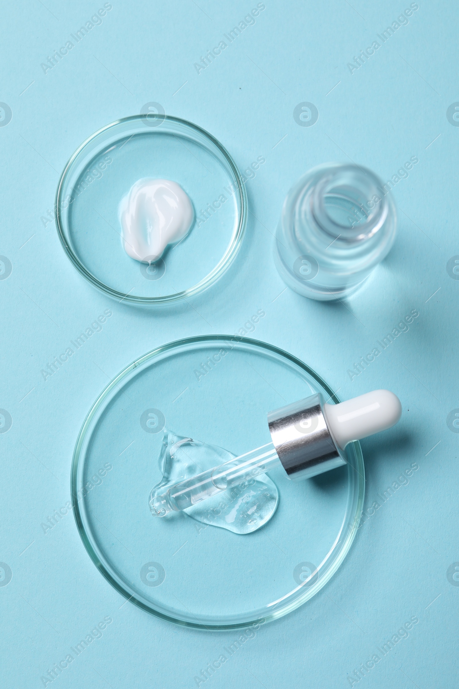 Photo of Petri dishes with samples of cosmetic serums, bottle and pipette on light blue background, flat lay