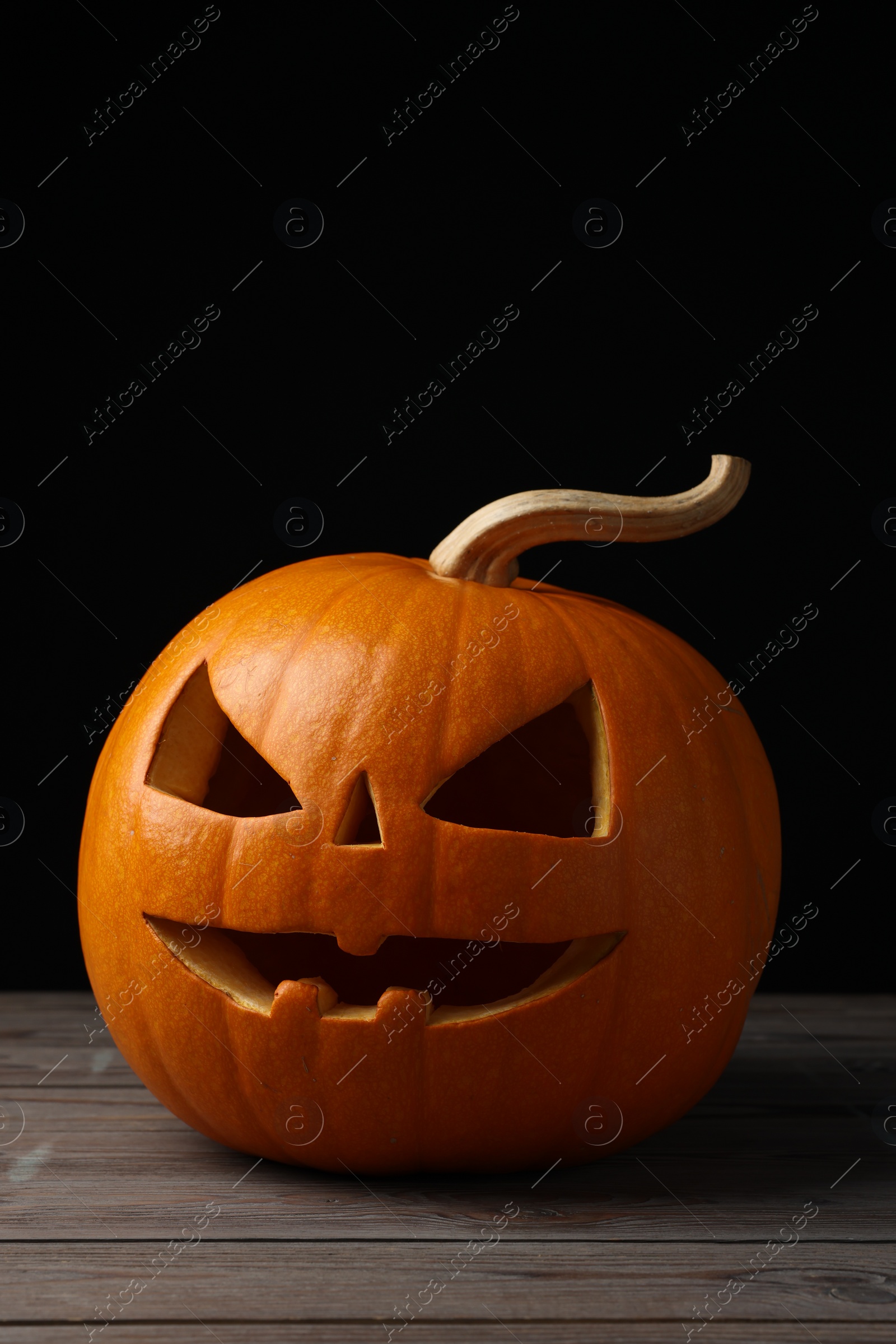 Photo of Scary jack o'lantern made of pumpkin on wooden table against black background. Halloween traditional decor