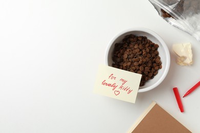 Photo of Flat lay composition with dry cat food and cute note on white table. Space for text
