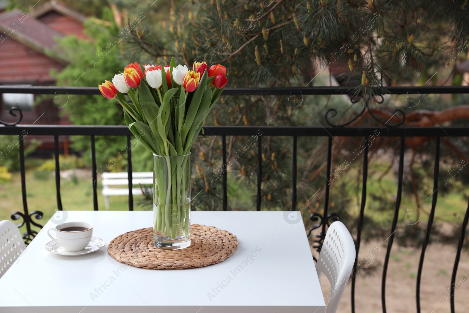 Photo of Beautiful colorful tulips in glass vase and cup of drink on white table at balcony, space for text