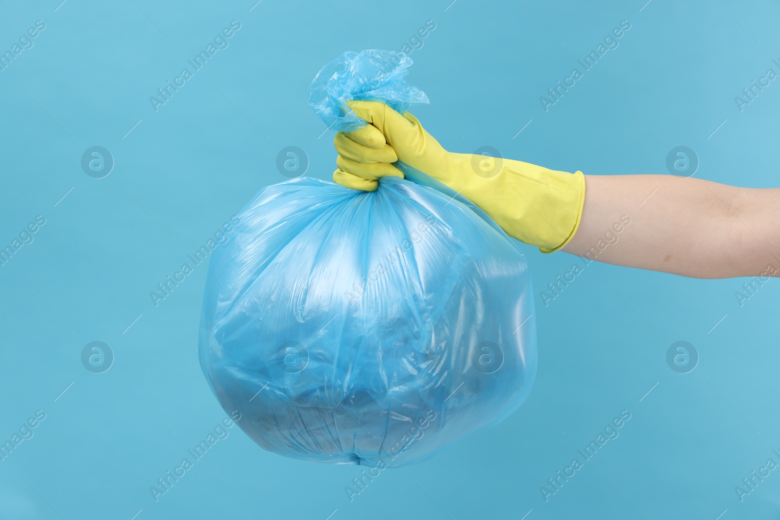 Photo of Woman holding plastic bag full of garbage on light blue background, closeup